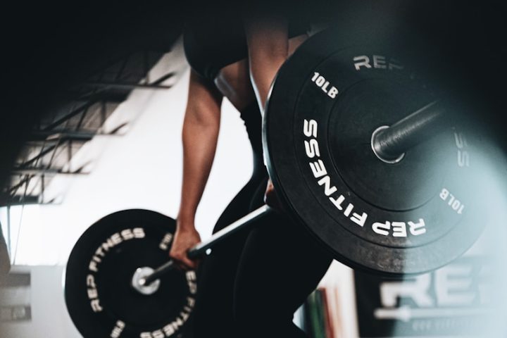 woman in black tank top and black leggings holding black barbell