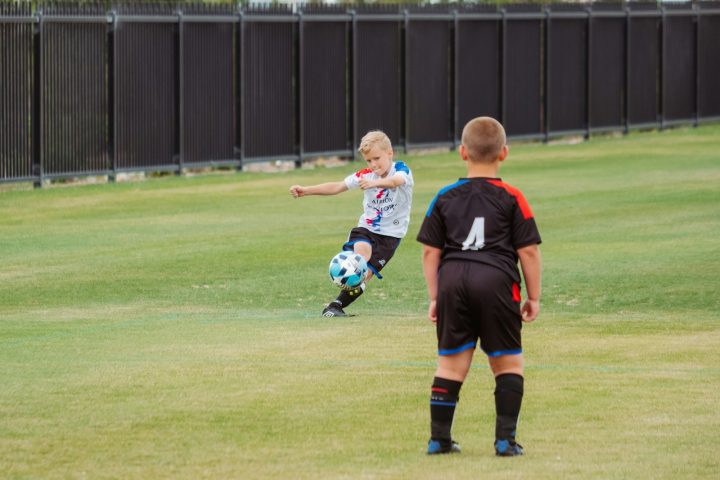 2 boys playing soccer on green grass field during daytime