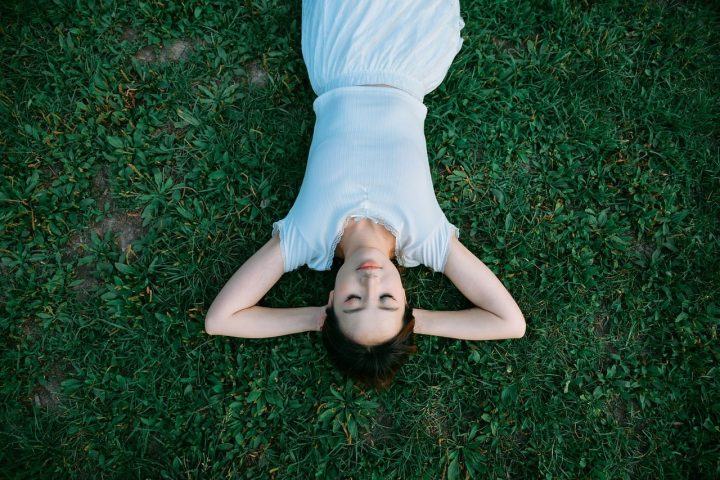 Jonge vrouw die ontspannen op het gras ligt en naar de lucht kijkt op een zomerse dag
